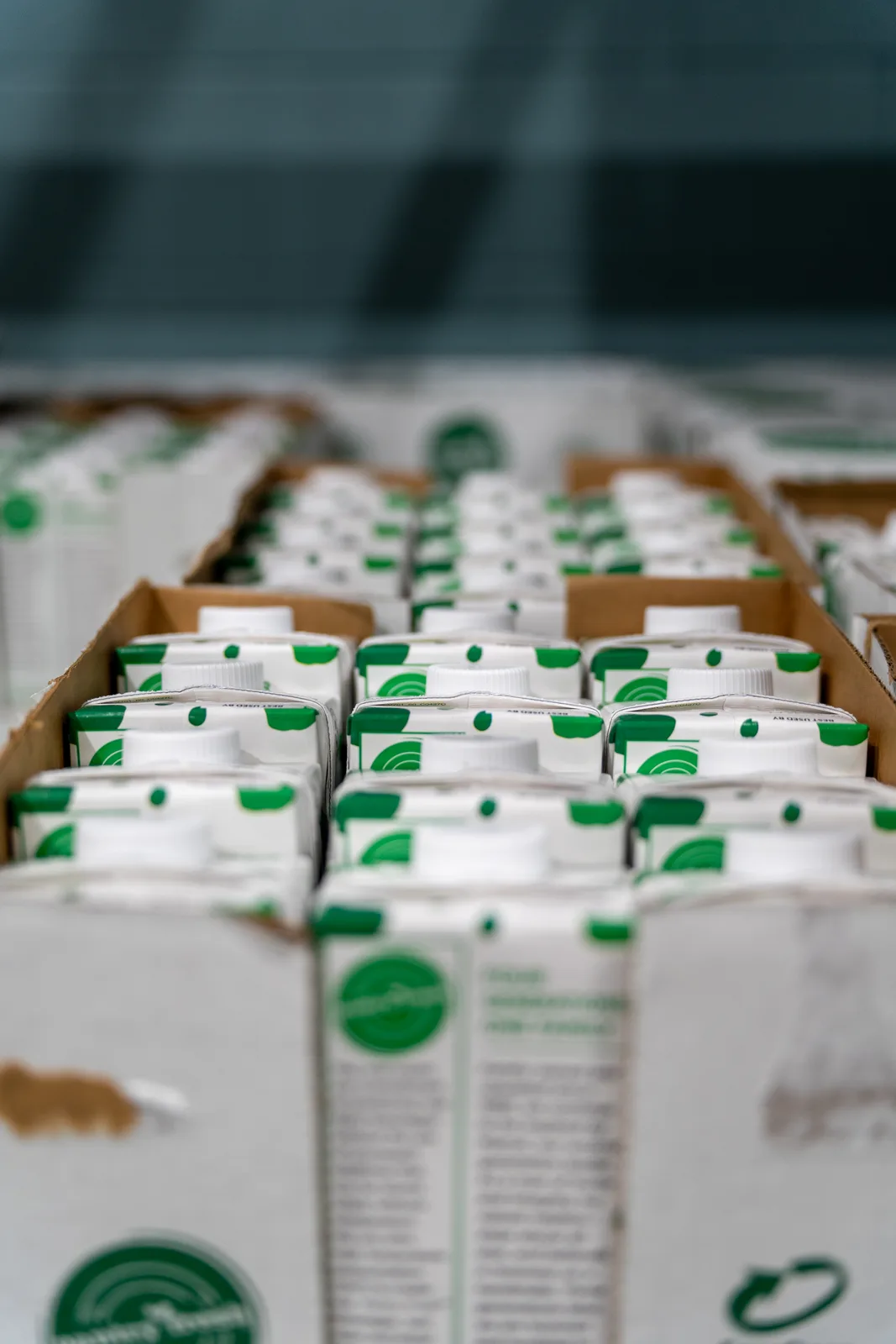 Rows of white milk cartons with green logos packed in cardboard boxes on warehouse shelves