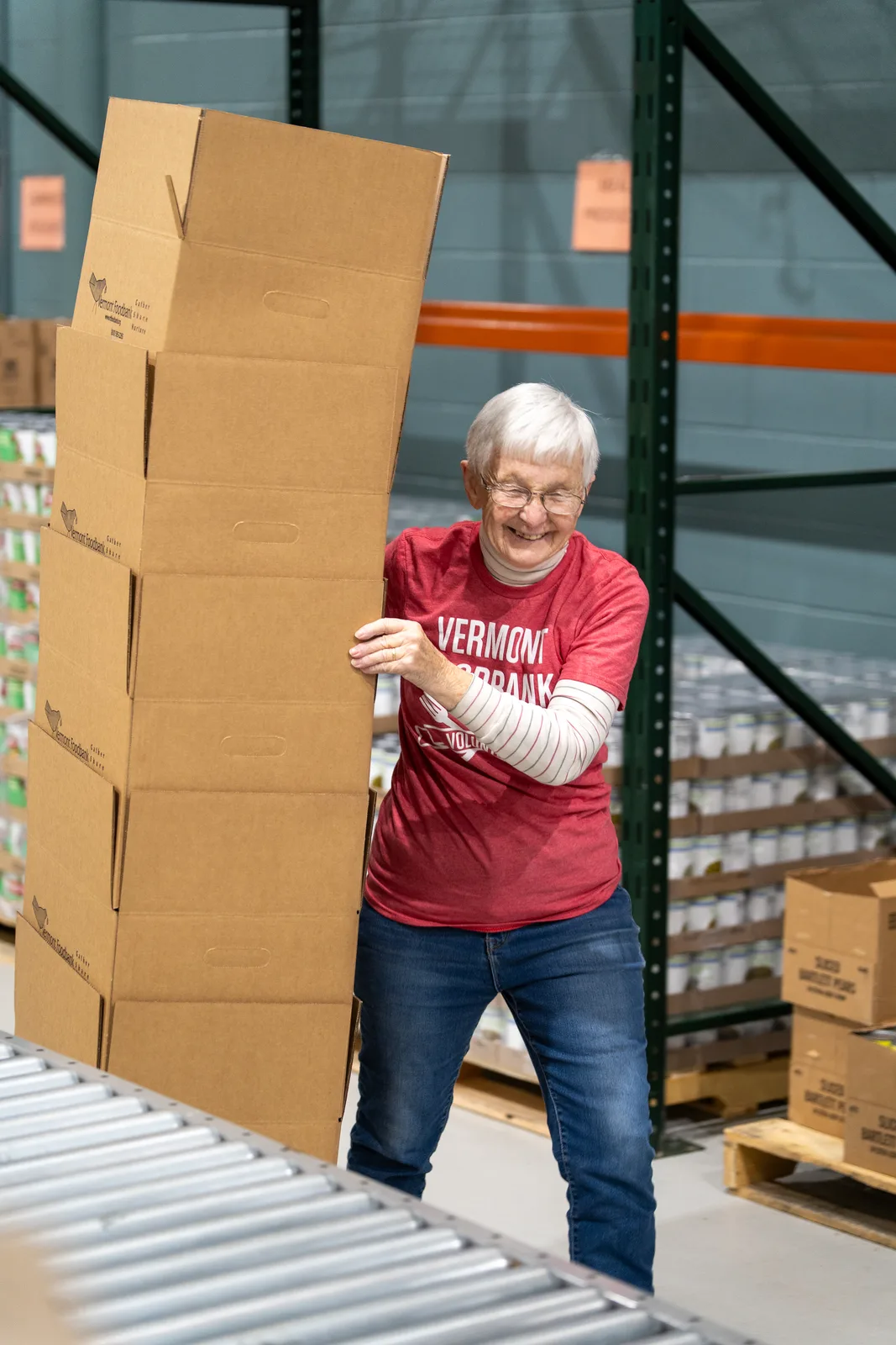 Person in red shirt holding stacked cardboard boxes near conveyor belt in warehouse