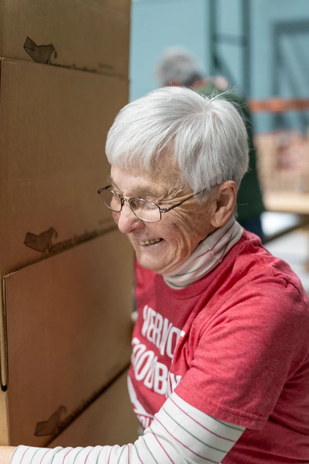 Person in red shirt smiling while working with cardboard boxes in warehouse