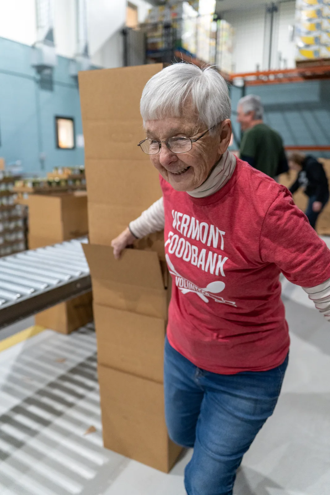 Person in red shirt leaning on stacked cardboard boxes near conveyor in warehouse