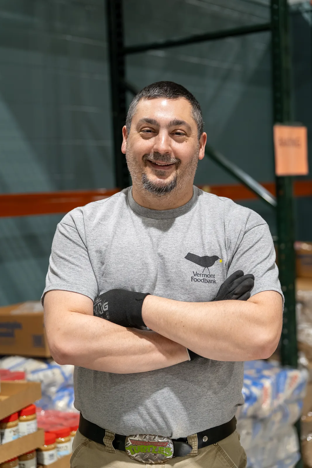 Person in gray shirt with black gloves standing in warehouse with shelves