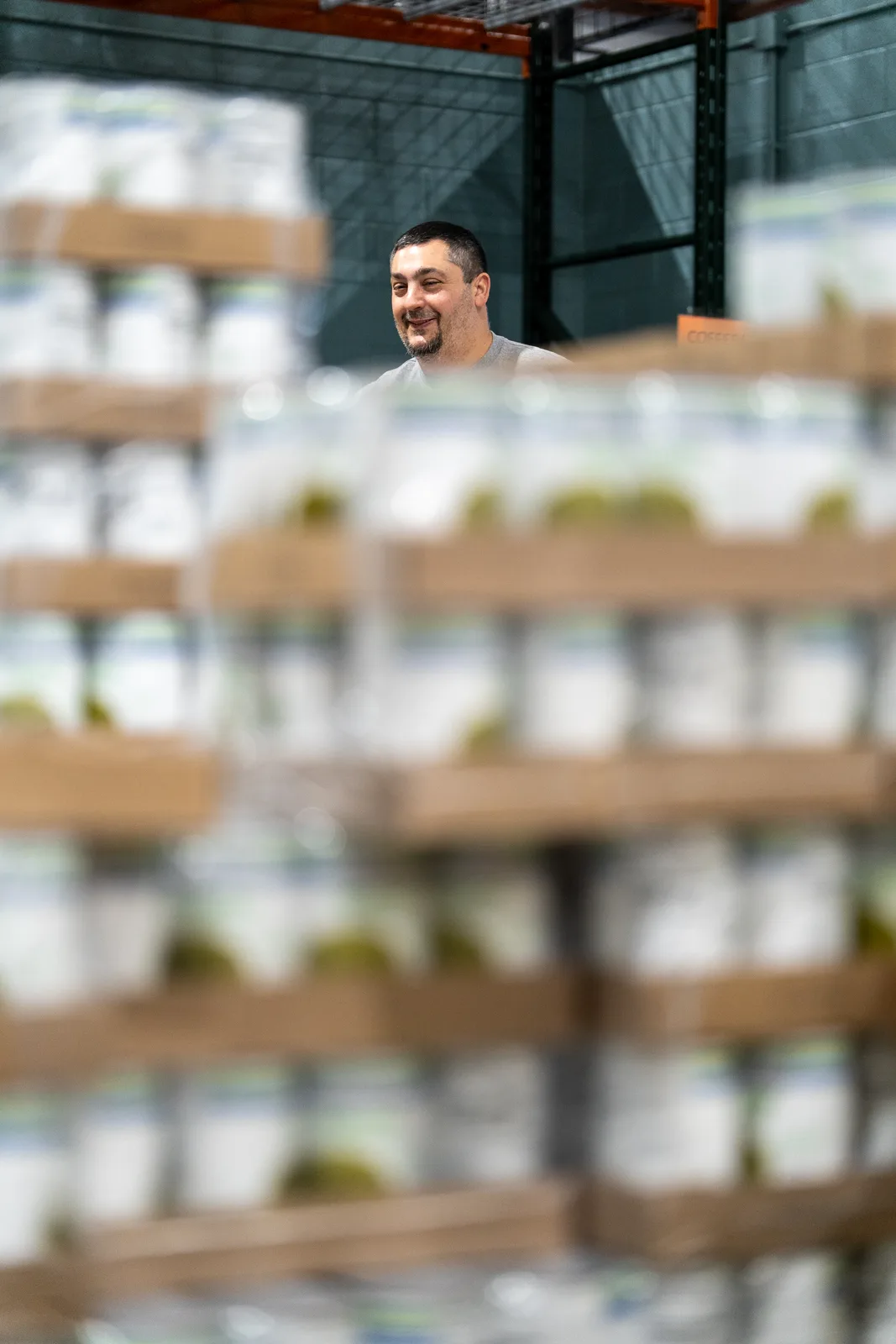 Person smiling behind shelves of plastic-wrapped canned goods in warehouse