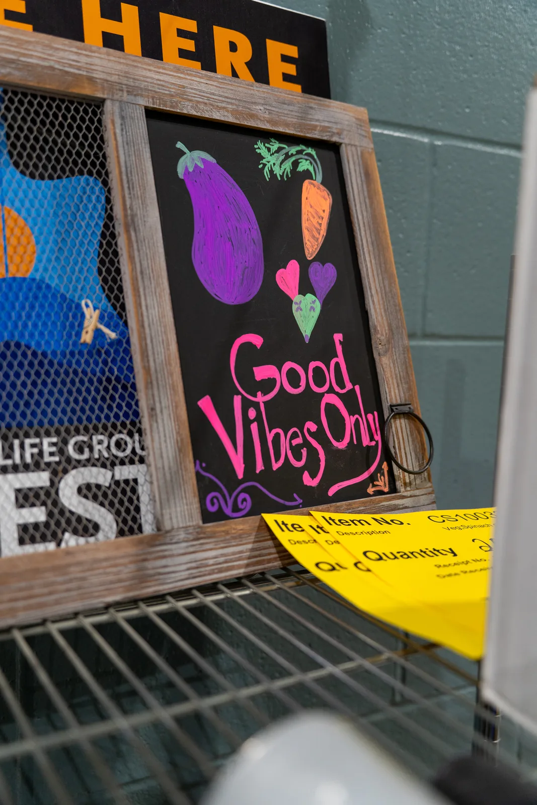 Chalkboard sign with colorful vegetables and text on metal shelving