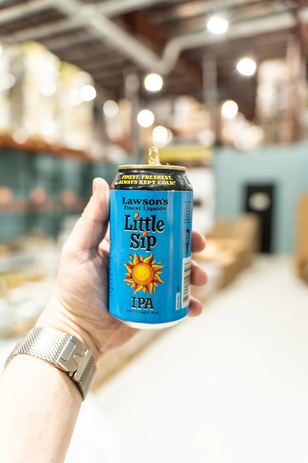 Hand holds a blue can of Lawson's Little Sip IPA inside the warehouse.