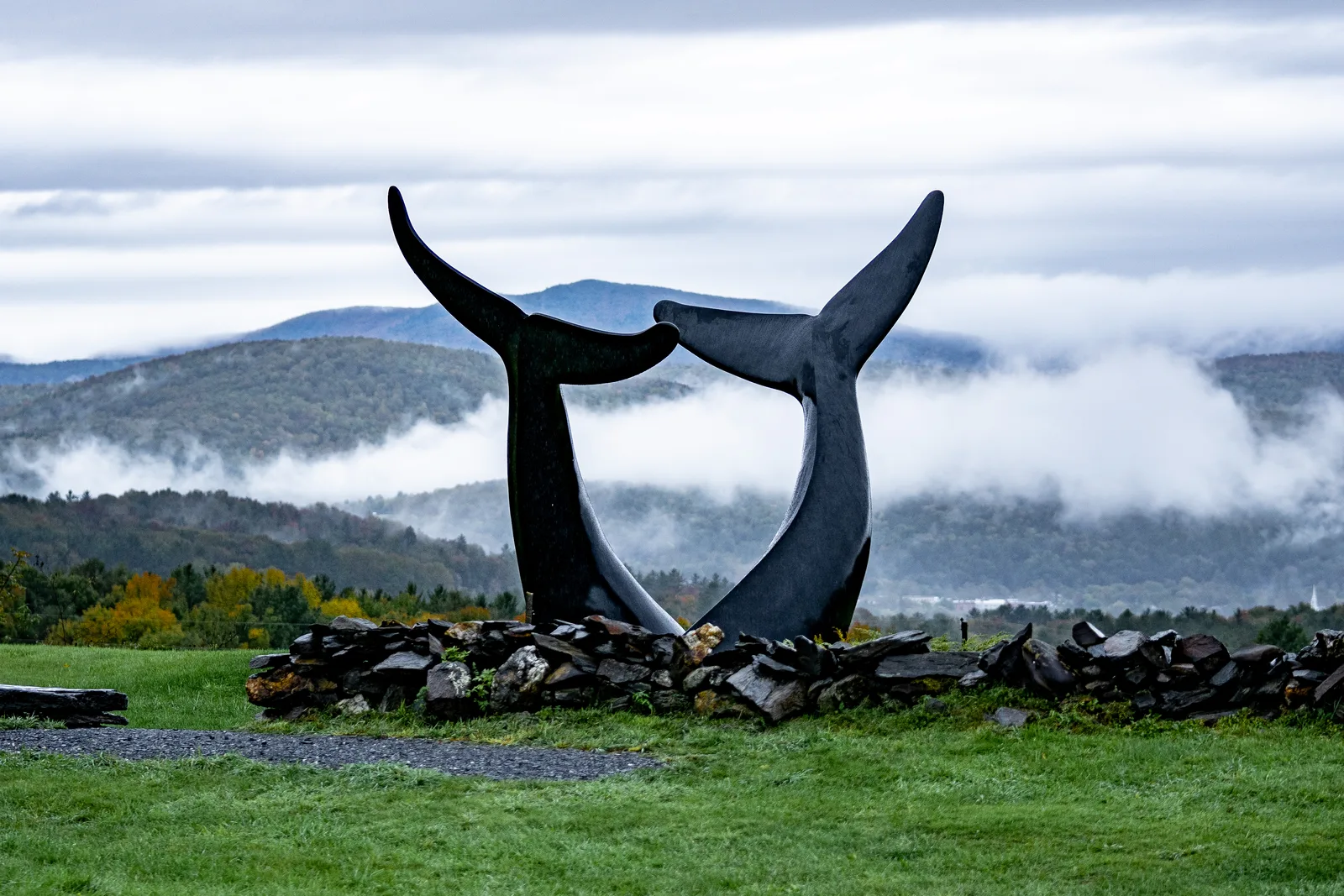 Jim Sardonis's Whale Dance sculpture above a stone wall with mist drifting through distant hills
