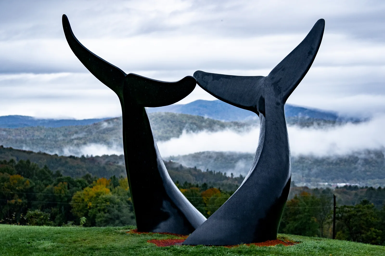 Bronze whale tails of Whale Dance silhouetted against layered hills and low clouds