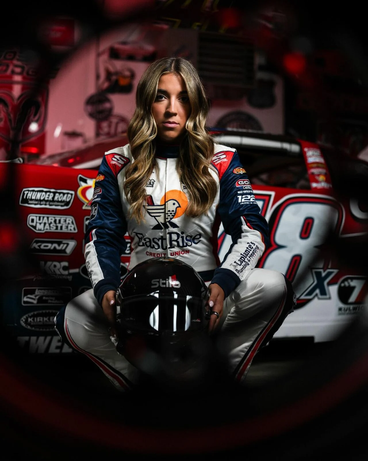 Race car driver Taylor Hoar poses in her EastRise racing suit with a helmet in front of her No. 48 car.