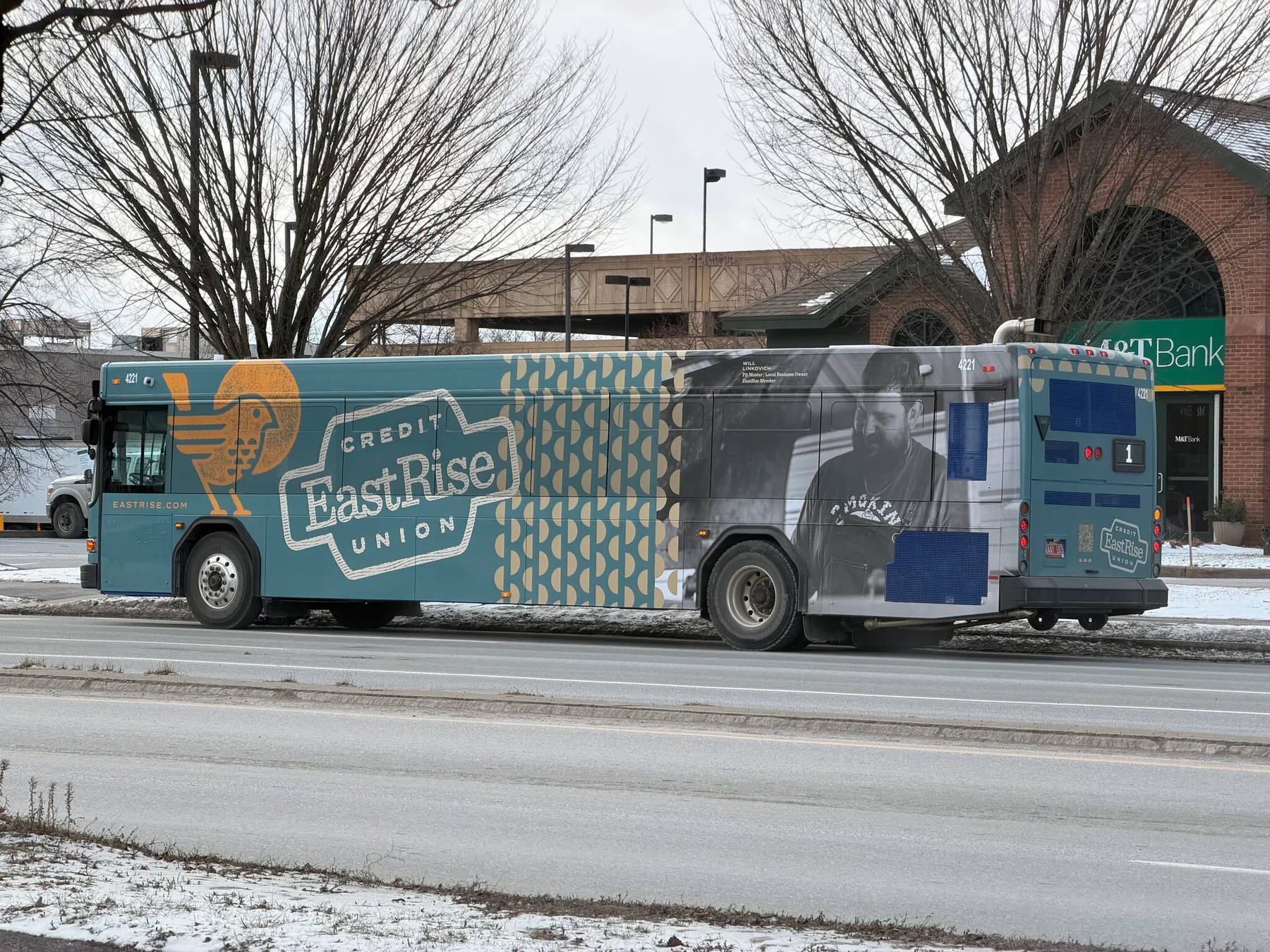 A city bus carries an EastRise Credit Union wrap featuring a member portrait and the credit union’s branding.