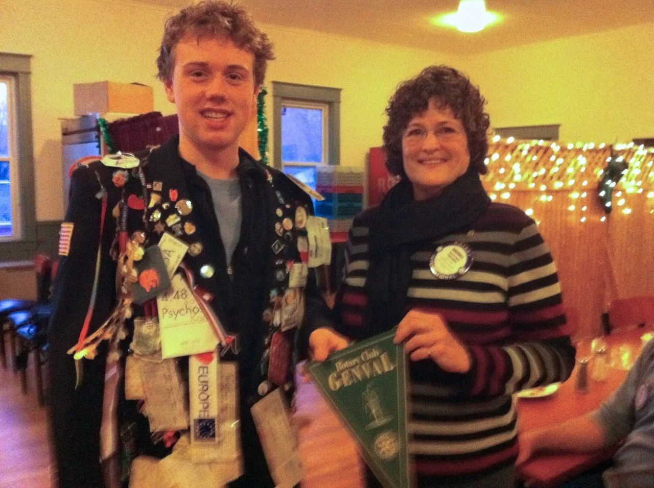 A teenage Oliver Ames wearing Rotary exchange pins stands beside a woman holding a Rotary gala program.