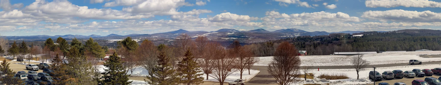 A panoramic office view shows snow-covered fields, wooded hills, and distant Vermont mountains beneath a blue sky.