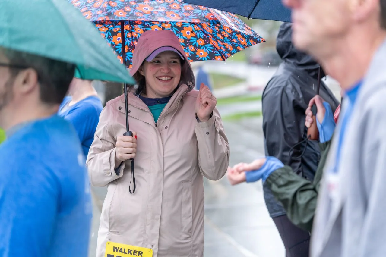 A smiling Corporate Cup participant in a pink coat stands beneath an umbrella.