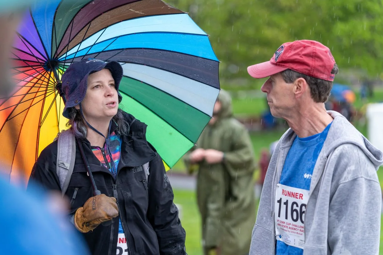Two Corporate Cup participants smile beneath a rainbow umbrella.
