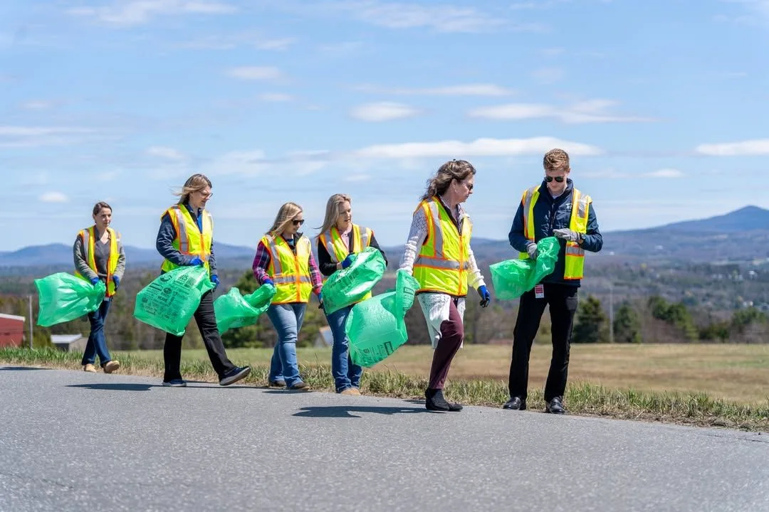Five volunteers pose with green cleanup bags beside a road.