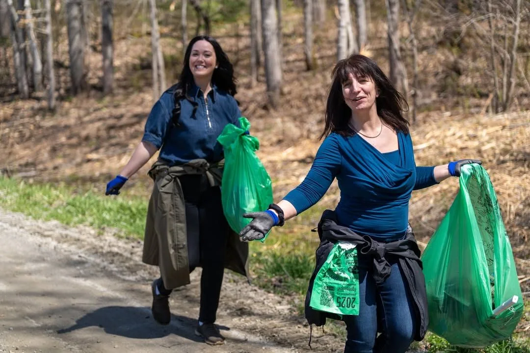 Two volunteers walk together carrying green cleanup bags.