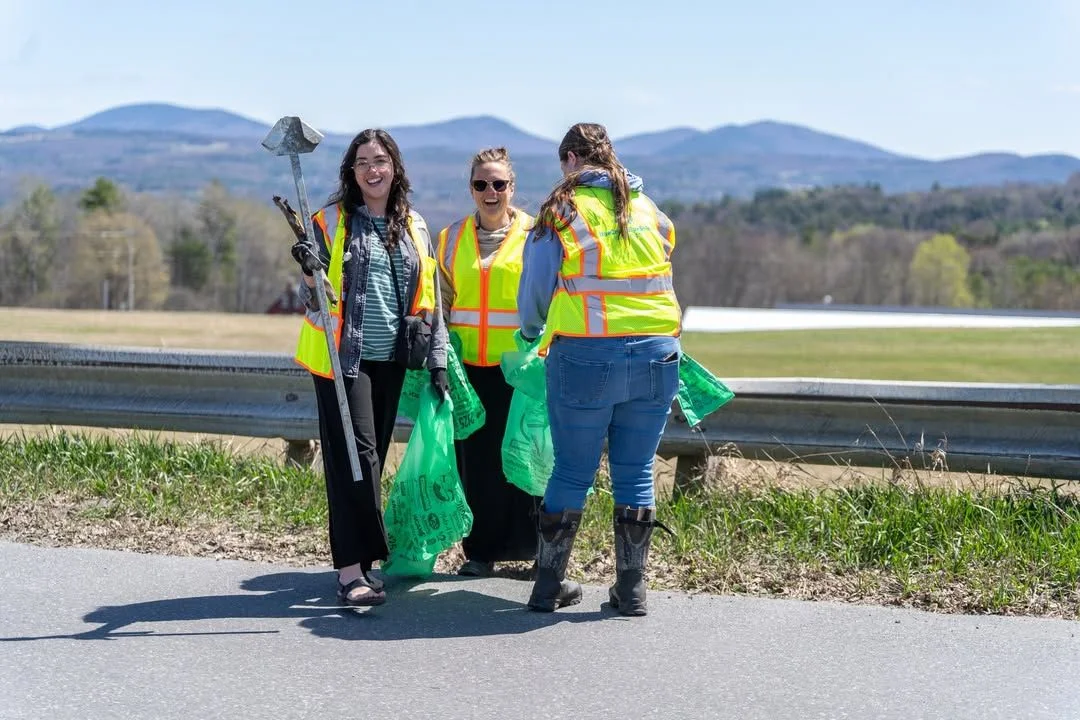 Four volunteers hold cleanup bags with Vermont mountains behind them.