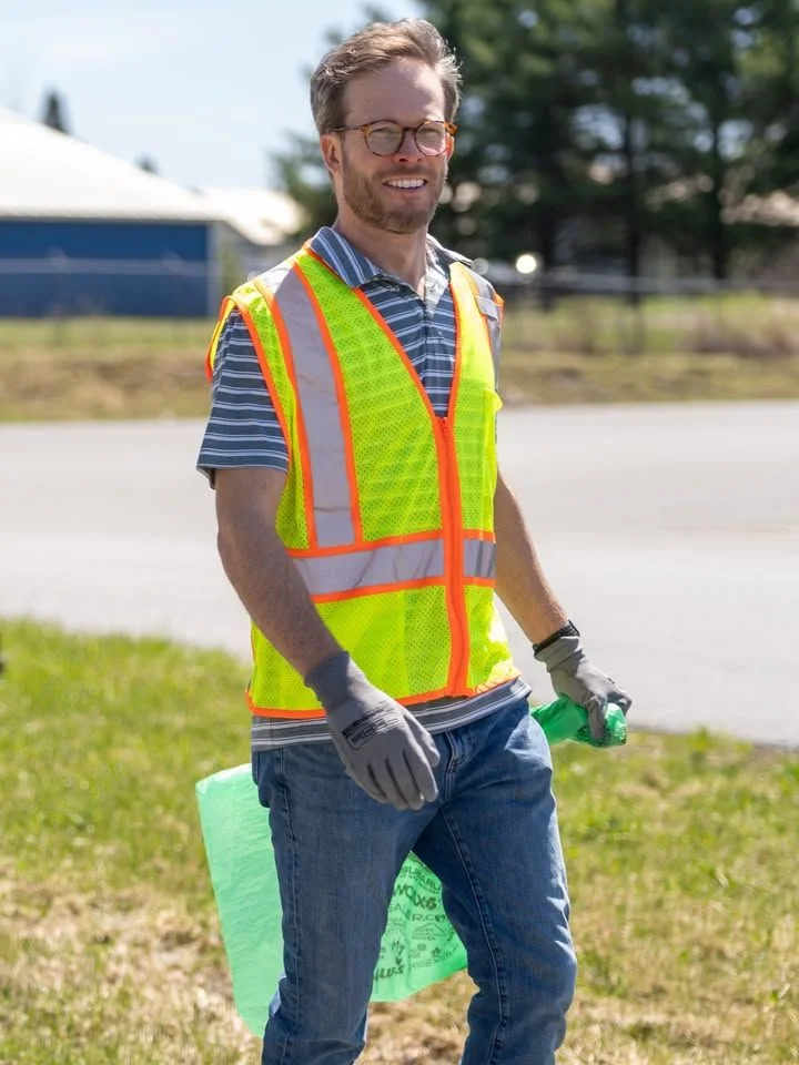 A volunteer in a striped shirt and safety vest pauses during Green Up Day.